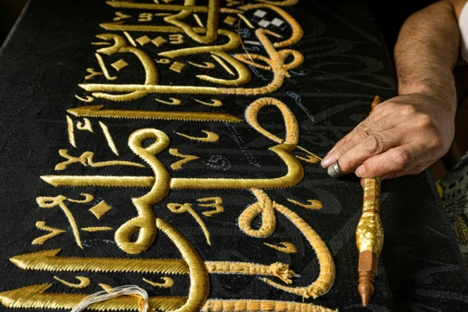 Un homme brode une épaisse étoffe noire de versets coraniques avec des fils d'or, le 15 juin 2022, au Caire