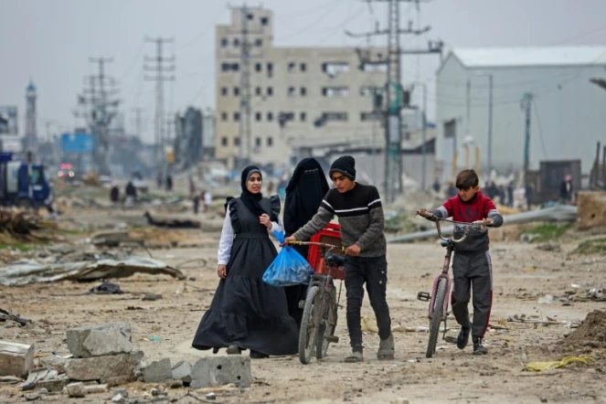 Des jeunes Palestiniens marchent autour des décombres dans le camp de réfugiés de Maghazi, dans le centre de la bande de Gaza, en partie détruit par les bombardemebnts israéliens, le 27 février 2024
