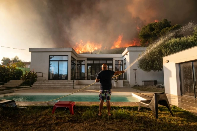 Un homme tente de maitriser le feu avant d'être évacué de sa maison à La Couronne, près de Marseille le 4 août 2020 où un violent incendie ravage l'ouest de la ville