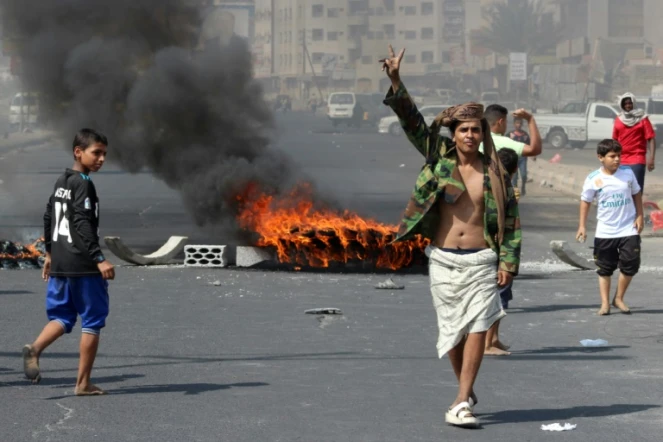 Un Yéménite fait le "V" de la victoire  en passant près de pneus incendiés lors de manifestations contre l'inflation et le coût de la vie, à Aden, dans le sud du Yémen, le 8 septembre 2018