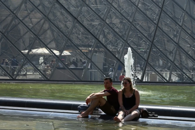 Des touristes se rafraîchissent dans un bassin devant la Pyramide du Louvre le 26 juin 2019