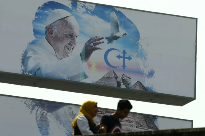 Des passants devant une affiche annonçant la visite papale, le 27 avril 2017 au Caire 