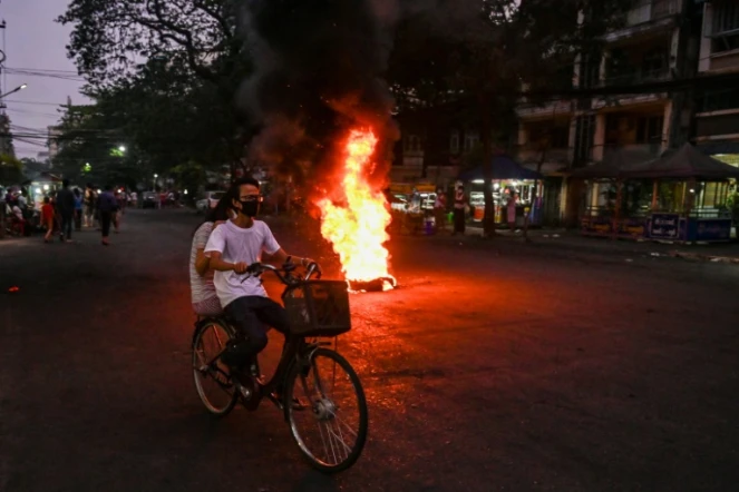 Des cyclistes passent près d'une barricade en flammes, érigée par des opposants à la junte militaire, le 3 avril 2021 à Rangoun
