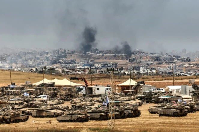 Des tanks et des bulldozers israéliens déployés à la lisière de la bande de Gaza, d'où s'élève de la fumée de bâtiments détruits par des frappes israéliennes, le 17 mai 2025