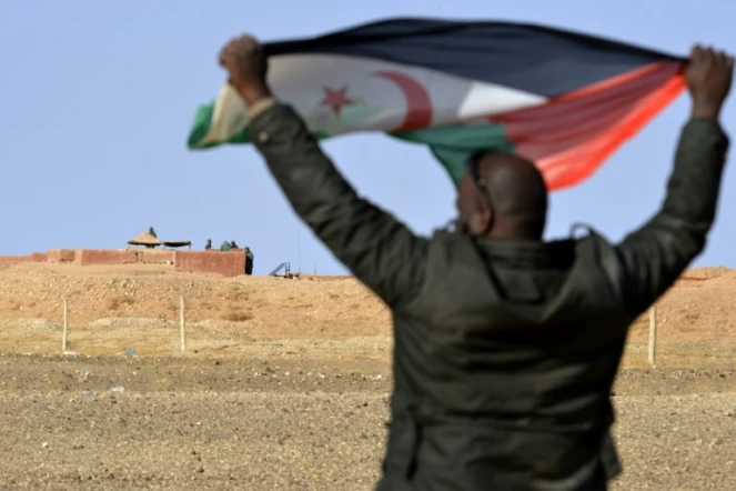 Un sahraoui brandit un drapeau du front polisario, non loin de soldats marocains surveillant le mur de défense au nord-ouest du territoire, près d'El-Mahbes, dans un secteur sous contrôle sahraoui, le 3 février 2017