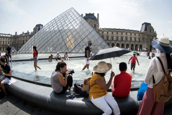 Touristes se rafraîchissant à la fontaine face à la pyramide du Louvre, à Paris le 7 août 2018