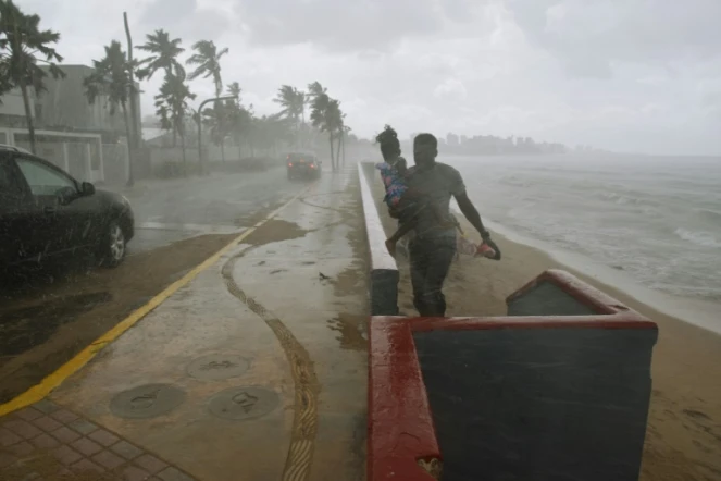 Un homme portant sa fille court pour échapper à la pluie et aux rafales de vent à l'approche de l'ouragan Maria, le 19 septembre 2017 à San Juan, à Porto Rico