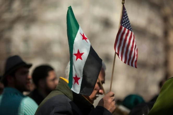 Un homme tient les drapeaux américains et syriens lors d'une manifestation devant la Maison Blanche le 15 mars 2014 