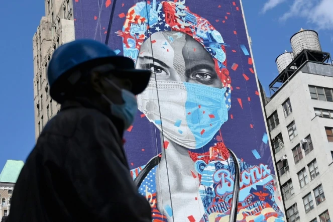 Un ouvrier masqué passe devant une fresque murale en l'honneur des soignants de la pandémie, le 7 mai 2020 à Manhattan