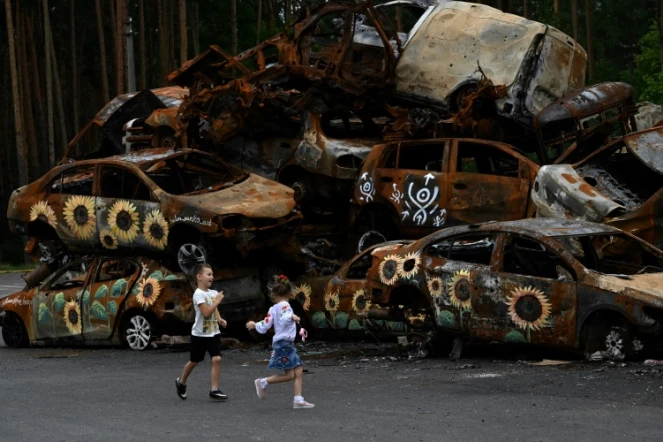 Des enfants jouent devant des carcasses de voitures calcinées, dont certaines ont été peintes par des artistes locaux, à Irpin le 9 août 2022