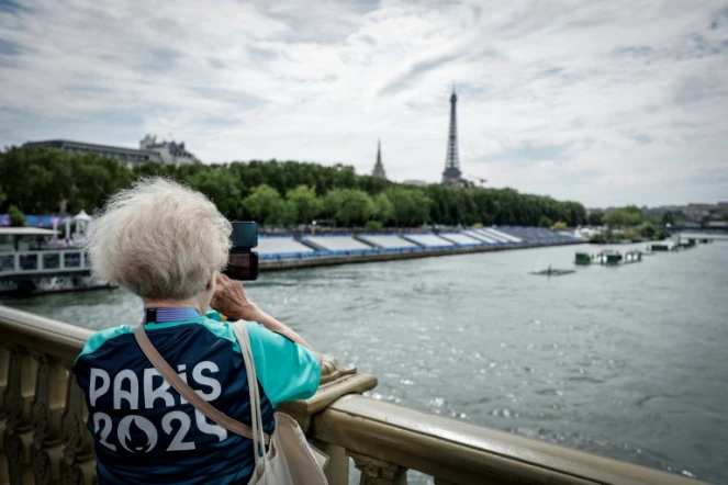 Une bénévole des JO-2024 prend une photo sur le pont des Invalides à côté des tribunes installées sur la Seine à la veille de la cérémonie d'ouverture des Jeux Olympiques 2024, à Paris, le 25 juillet 2024