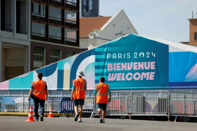 Des membres de l'organisation des JO-2024 marchent près de l'entrée du village des athlètes, le 18 juillet 2024 à Saint-Denis en Seine-Saint-Denis