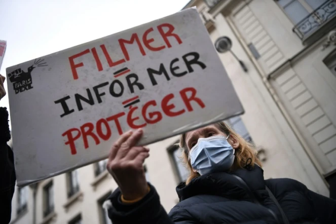 Une manifestante tient une pancarte "filmer = informer = protéger" durant une manifestation contre la loi sécurité globale devant le Sénat le 16 mars 2021