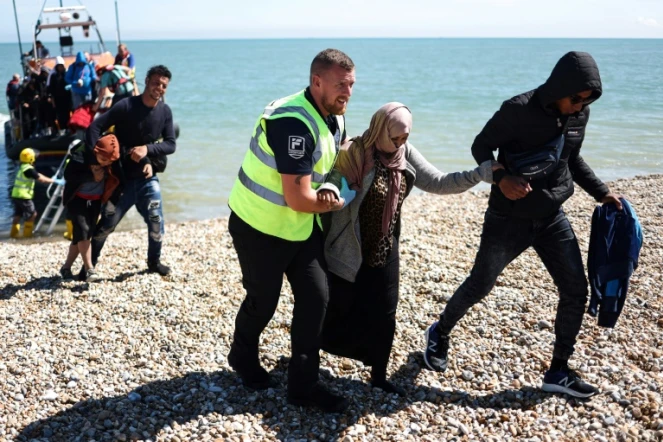 Un officier interforce aide une femme migrante sur la plage de Dungeness, sur la côte sud-est de l'Angleterre, le 16 août 2023