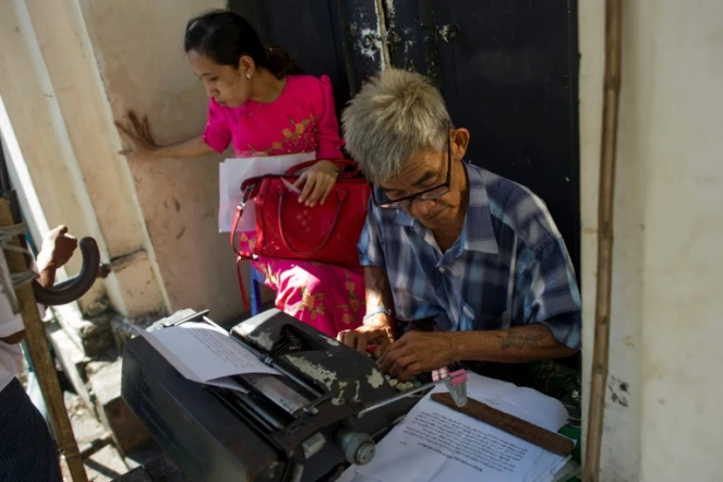 Aung Min, un des rares écrivains publics restant dans la capitale birmane Rangoun, travaille sur le document d'une cliente dans la rue Pansodan, le 5 décembre 2018