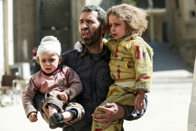 Un Syrien tient dans ses bras deux enfants blessés après une frappe aérienne à Hamouria près de Damas qui a fait au moins 16 civils morts et des dizaines de blessés le 25 mars 2017