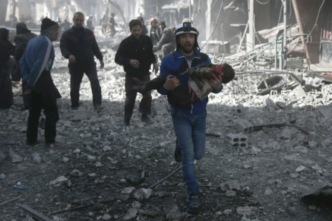 Un secouriste des zones rebelles syriennes en train de secourir un enfant blessé après de violents bombardement du régime sur la ville insurgée de Hammouriyé, le 19 février 2018 