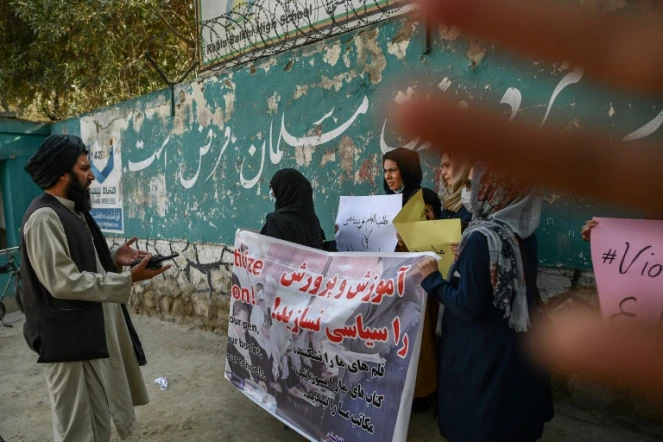 Un membre des talibans parle à des manifestantes devant une école à Kaboul le 30 septembre 2021 tandis qu'un autre tente de cacher l'objectif de l'appareil photo 