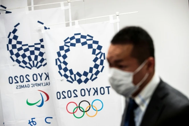 Un homme porte un masque à côté des logos des Jeux olympiques et paralympiques de Tokyo-2020 le 11 mars 2020 à Tokyo (Japon)
