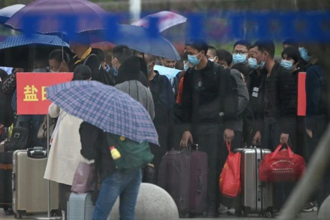 Des personnes portant un masque de protection font la queue pour acheter un billet de train à la gare de Macheng, le 25 mars 2020 dans la province chinoise du Hubei