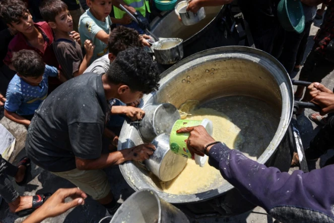 Des enfants palestiniens tentent de prendre ce qui reste dans un récipient de soupe aux lentilles dans un point de distribution de nourriture dans la ville de Gaza, le 25 juillet 2025