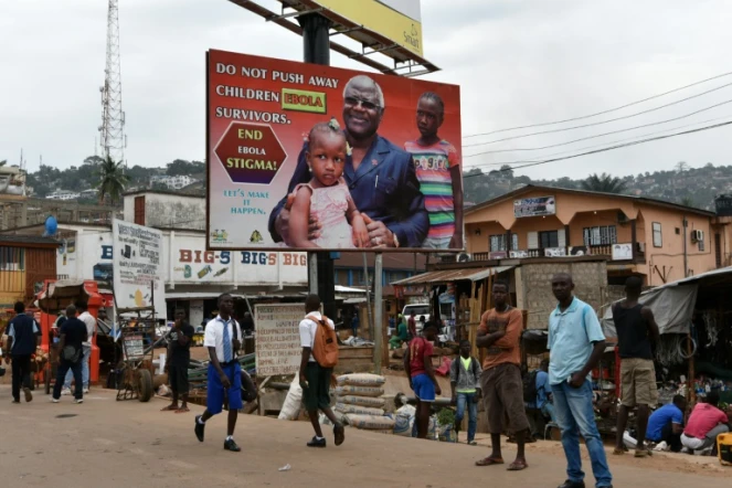 Des habitants de Freetown en Sierra Leone marchent sous une affiche de campagne contre Ebola représentant le président Ernest Bai Koroma