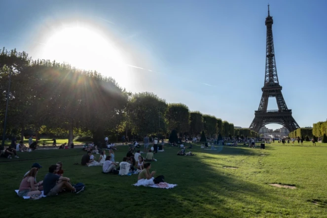 Des personnes profitent de l'ombre sur les pelouses du Champs de Mars, devant la Tour Eiffel, à Paris, pendant un épisode de canicule, le 21 août 2023 