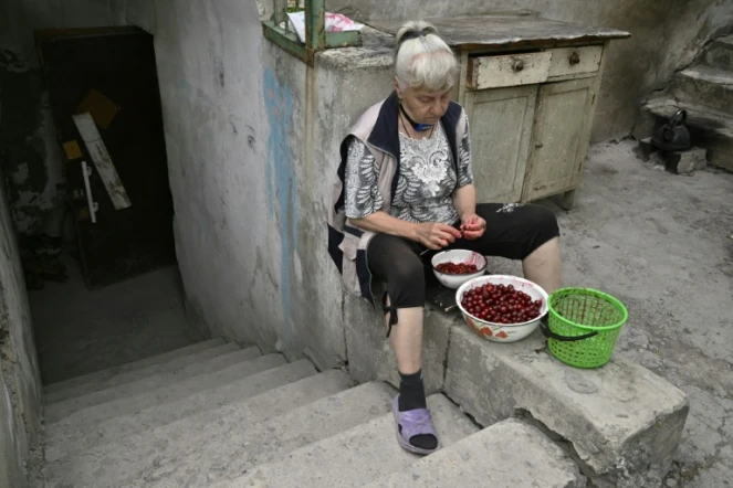 Lioudmila, assise devant l'entrée d'un sous-sol servant d'abri, dénoyaute des cerises, le 30 juin 2022 à Seversk, dans la région de Donetsk, en Ukraine