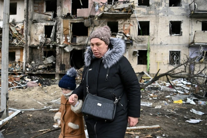 Une femme avec un enfant marche devant un immeuble résidentiel endommagé dans la rue Koshytsa, une banlieue de la de  Kiev, le 25 février 2022.