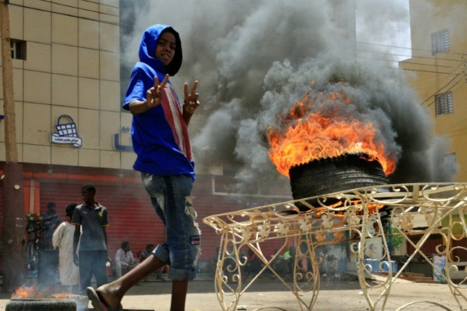 Un manifestant soudanais fait le "V" de la victoire devant un pneu en flammes, le 3 juin 2019 près du siège de l'armée à Khartoum