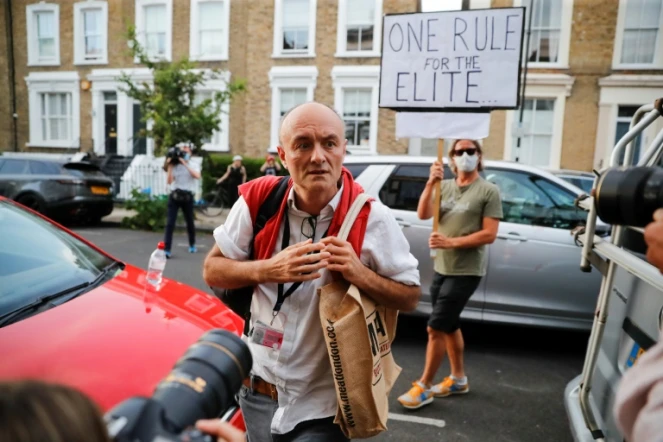 Dominic Cummings, le conseiller du Premier ministre Boris Johnson, à son arrivée chez lui à Londres, le 25 mai 2020, alors qu'une manifestante brandit une pancarte qui dit "Une règle à part pour les élites"