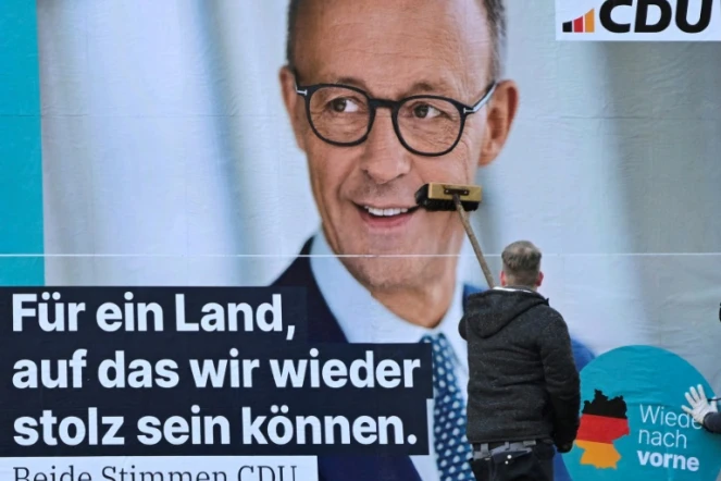 Un homme colle une affiche de Friedrich Merz, leader des conservateurs allemands et favori à la chancellerie, le 13 janvier 2025 à Berlin, en vue des élections législatives anticipées du 23 février