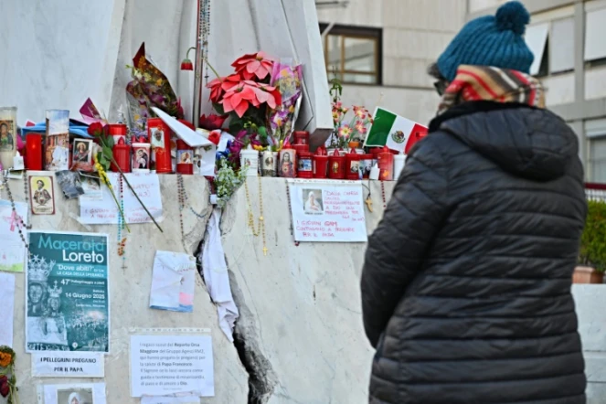 Une personne prie devant la statue de Jean-Paul II à l'extérieur de l'hôpital Gemelli à Rome où est soigné le pape François pour une pneumonie, le 6 mars 2025