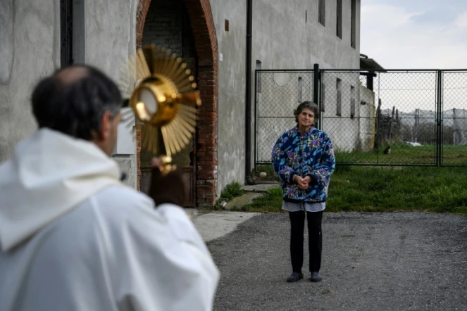 Le père Don Kresimir Busic prie avec une paroissienne à Manta, dans le Piedmont, dans le nord de l'Italie, dans le cadre d'une procession religieuse pour bénir les maisons contre le coronavirus, le 25 mars 2020 