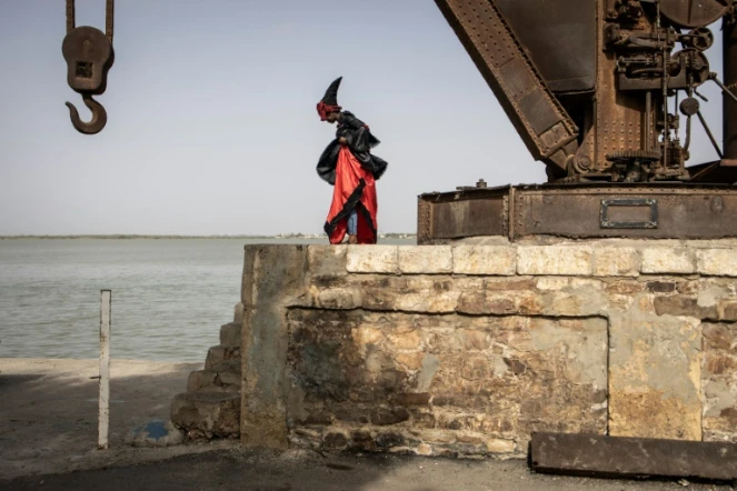 Un mannequin marche devant une grue portuaire désaffectée, vêtu d'une tenue traditionnelle des Signares à Saint Louis, le 10 août 2021