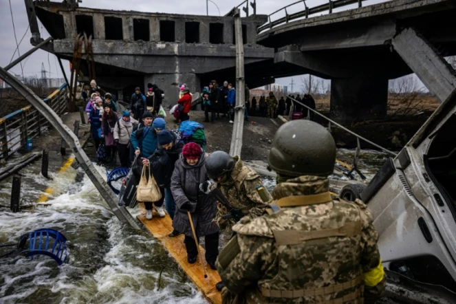 Des personnes évacuées traversent un pont détruit pour quitter la ville d'Irpin, au nord-ouest de Kiev, le 7 mars 2022.