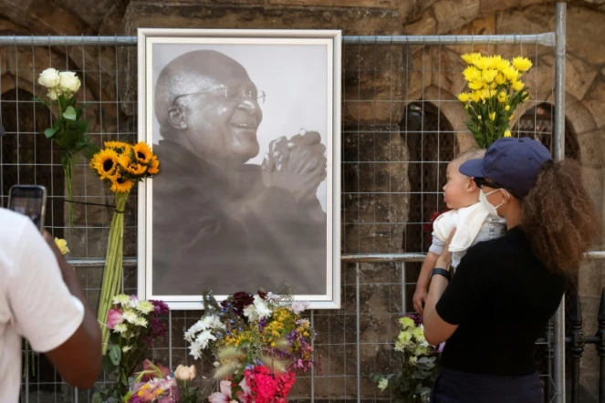 Des personnes déposent des fleurs auprès de l'effigie de Desmond Tutu accrochée devant la cathédrale Saint-Georges au Cap, le 26 décembre 2021