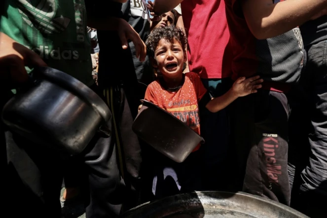 Un enfant pleure au milieu de Palestiniens qui attendent de recevoir un repas chaud distribué par une association caritative locale à Nousseirat, dans le centre de la bande de Gaza, le 24 mai 2025