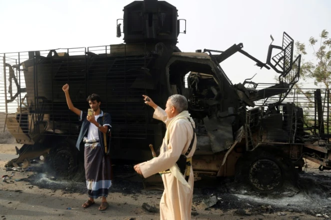 Des hommes armés yéménites inspectent un véhicule détruit après des affrontements entre forces loyalistes et rebelles près du port de Hodeida (ouest), cible d'une offensive du pouvoir aidé par l'Arabie saoudite et les Emirats, le 29 mai 2018