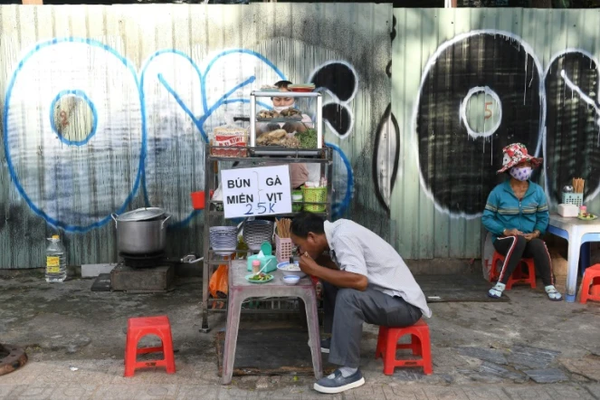Un homme déjeune d'un bol de soupe aux nouilles sur l'étal d'une vendeuse de rue, le 8 septembre 2020 à Ho Chi Minh-Ville, au Vietnam