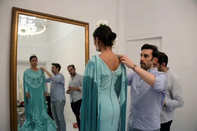 Le couturier espagnol Luis Fernández (c) ajuste une robe de flamenco sur sa cliente Virginia Cuaresma, dans son atelier de Séville, le 8 avril 2024