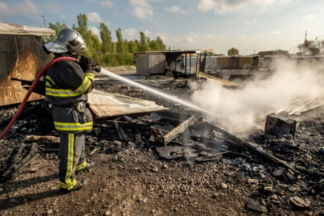 Un pompier arrose les décombres de maisons détruites par un incendie dû à des rixes entre Afghans et Kurdes dans le camp de migrants de Grande-Synthe le 11 avril 2017 à Dunkerque