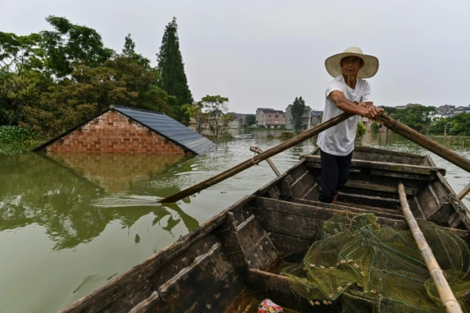 Un pêcheur passe en barque près d'une habitation dont n'émerge que le toit, dans le village de Longkou, dans la région de Poyang qui a subi des pluies violentes, dans la province du Jiangxi, au centre de la Chine, le 16 juillet 2020