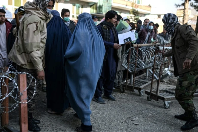 Deux femmes en burqa quittent le bureau des passeport dont l'entrée est contrôlée par des talibans, le 18 décembre 2021 à Kaboul