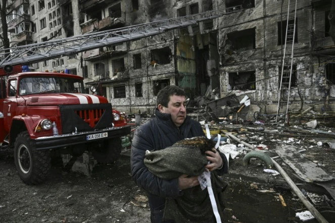 Un homme porte son chat mort devant un immeube d'habitation détruit près de Kiev, le 14 mars 2022