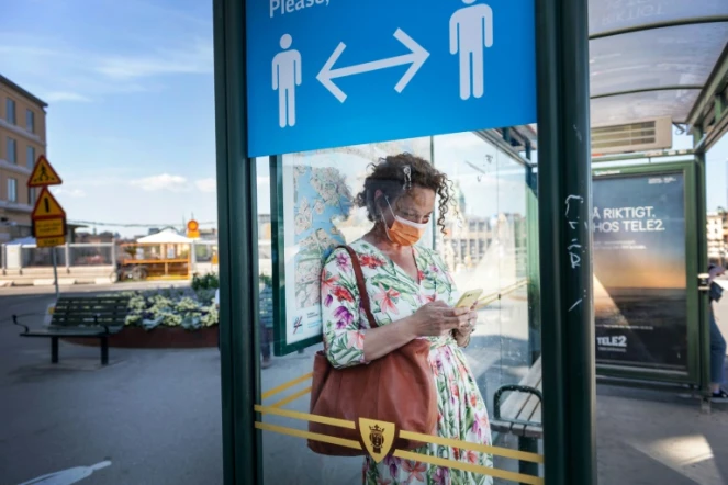 Une passante à Stockholm, le 26 juin 2020 devant une affiche recommandant la distanciation sociale