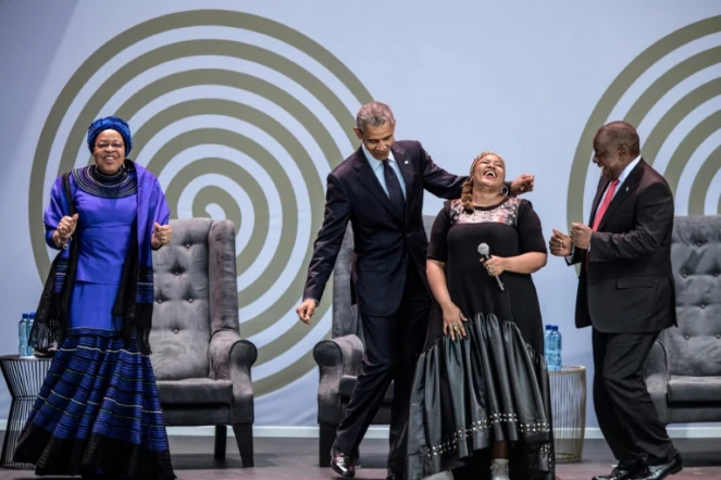 L'ex président américain Barack Obama, la veuve de Nelson Mandela, Graça Machel (à gauche) et le président sud-africain Cyril Ramaphosa (à droite) dansent en compagnie de la chanteuse Thandiswa Mazwai lors d'une cérémonie en l'honneur de Mandela, le 17 juillet 2018 à Johannesbourg