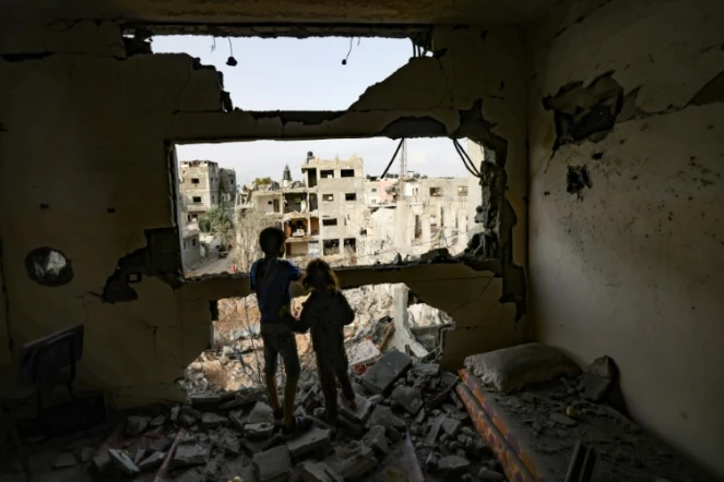 Des enfants dans les ruines d'un immeuble regardent les bâtiments détruits par des frappes israéliennes, le 21 mai 2021 à Gaza