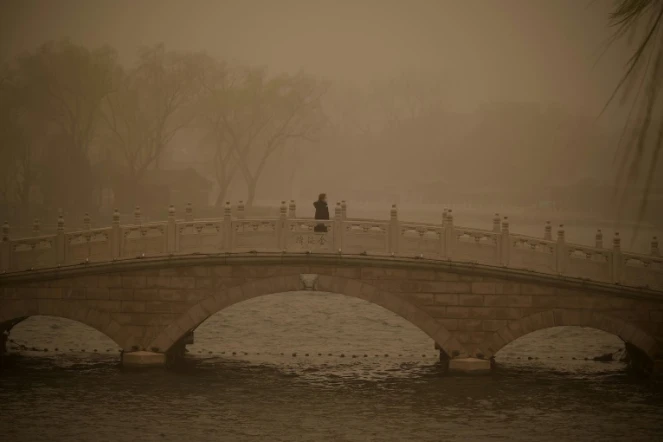 Une femme traverse un pont pendant une tempête de sable à Pékin le 15 mars 2021