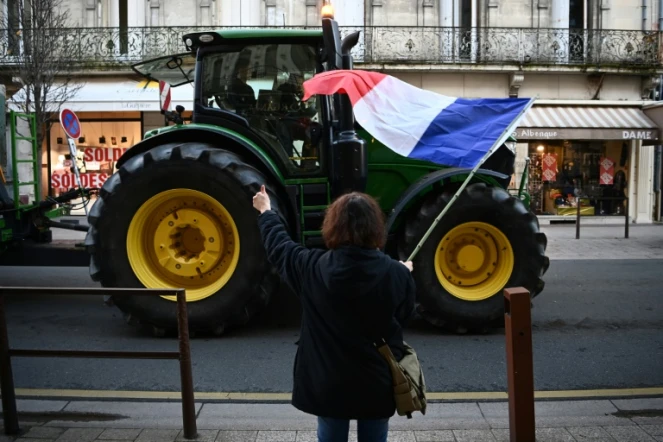 Un agriculteur manifeste avec son tracteur, salué par une passante avec un drapeau français, à Agen, dans le Lot-et-Garonne, le 25 janvier 2024